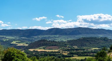 Parlak mavi gökyüzünün altındaki İspanyol kırsalının kayan tepelerini ve yamalı arazilerini manzarası. Yeşil ve kahverenginin tonları, kabarık beyaz bulutlarla çok güzel tezat oluşturuyor..