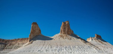 Erimiş kumtaşı sütunları, berrak mavi gökyüzünün altında çorak bir çöl zemininden çarpıcı bir şekilde yükseliyor, kuru ve uzak bir arazide jeolojik oluşumlar sergiliyorlar..