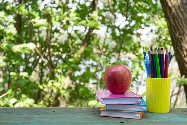 Blurry outdoor background for education and back to school concept. School supplies and apple on wooden table on natural background