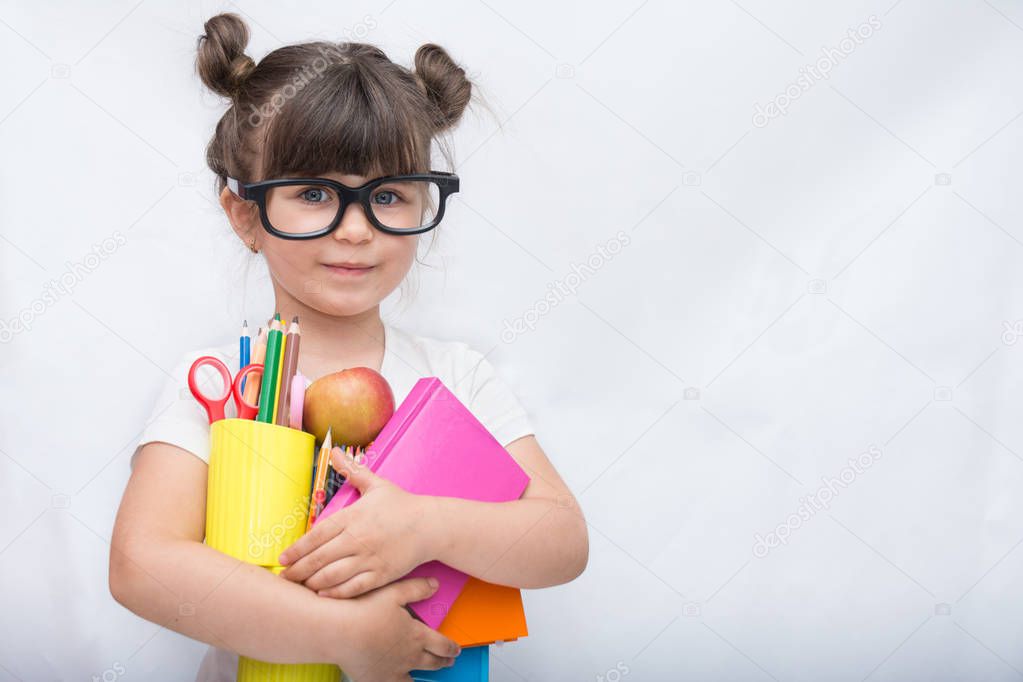 Kid ready for school. Cute clever child in eyeglasses holding school supplies: pens, notebooks, scissors and apple. Back to school concept. Space for text, isolated on white.