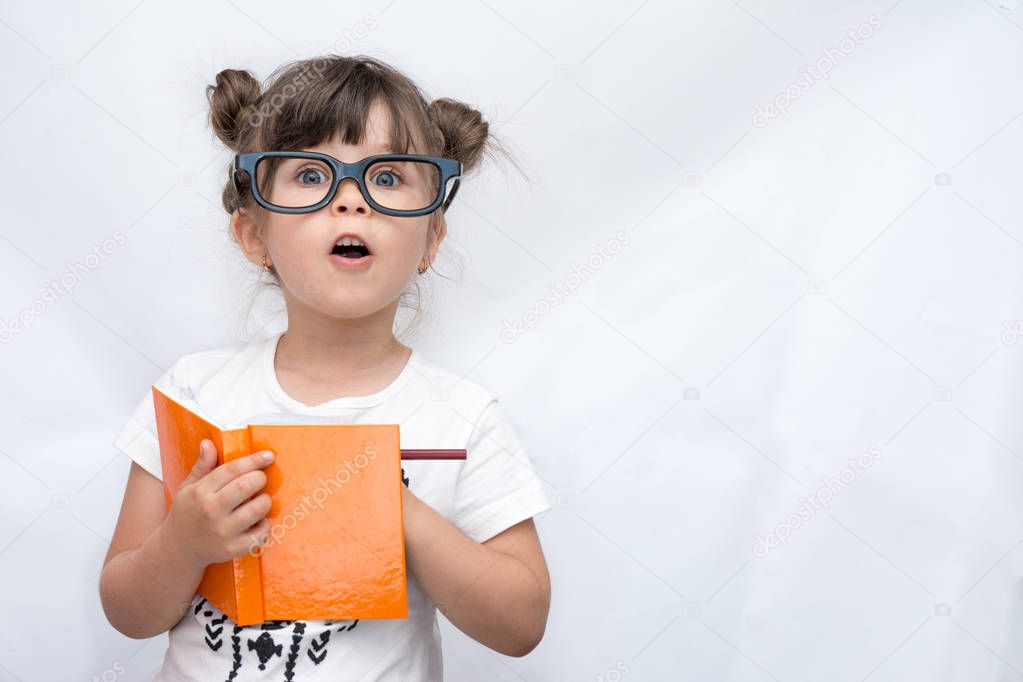 Surprised cute child in eyeglasses, writing in notebook using pencil, keeping mouth wide open. Four or five years old kid, isolated on white, space for advertising text