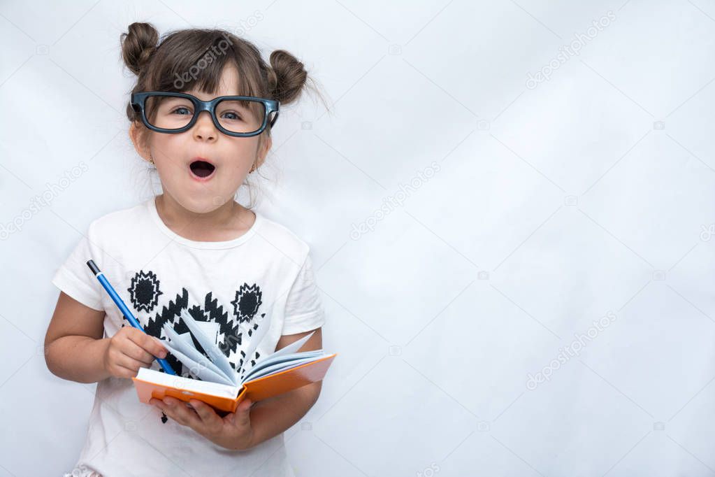 Surprised cute child in eyeglasses, writing in notebook using pencil, keeping mouth wide open. Four years old kid, isolated on white, space for advertising 