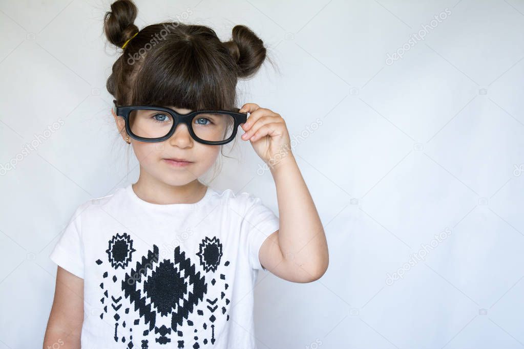 Stylish girl in glasses. Happy small brunette kid with blue eyes looking in camera with happy and peaceful expression. Copy space, isolated on white background