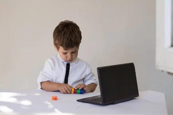 Child  sitting in front of a laptop  and counting his play money in office. Kid saving money for the future. Financial responsibility and education concept.