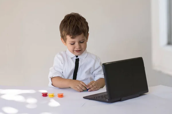 Child  sitting in front of a laptop  and counting his play money in office. Kid saving money for the future. Financial responsibility and education concept.