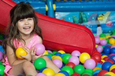 Mutlu gülen kız çocuk kapalı oyun merkezinde eğleniyor. Bahçesi top bilardo renkli topları ile oynayan çocuk. Tatil