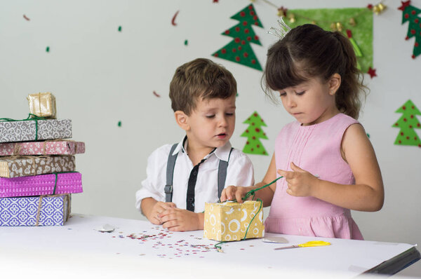 Cute happy excited children, boy and girl open christmas present box in beautiful room. Sister and brother give Xmas gifts near decorated tree. Family holiday
