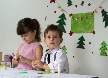Çocuk erkek ve kız Noel için dekorasyon yapıyor. Yeni yıl süslemeleri içinde güzel duygusal samimi yürümeye başlayan.