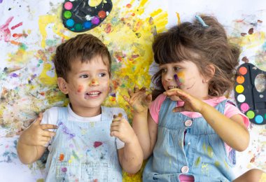 Renk ile gülen çocuklar nokta renkler ve renk yerde yatarken fırçalar ile yüzündeki boya. Çocuk açık resim.