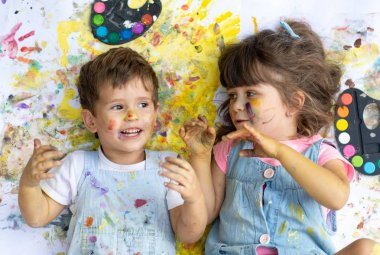 Nokta renkler ve fırçalar yerde yatarken yüzünde renk ile gülen çocuk boya.
