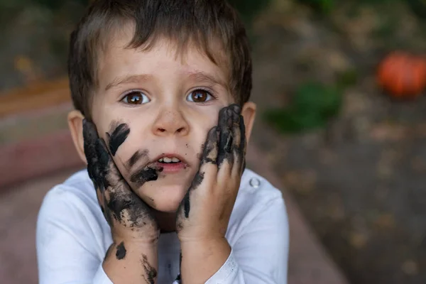 Funny kid, mud dirty face. Happy pretty kid boy playing outside with dirty hands and face.