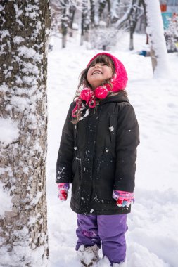 Küçük kız ceket ve örme şapka Noel'de kar taneleri kış Park yakalamak. Çocuklar karlı ormanda oynar. Kışın kar ile oynayan çocuk.