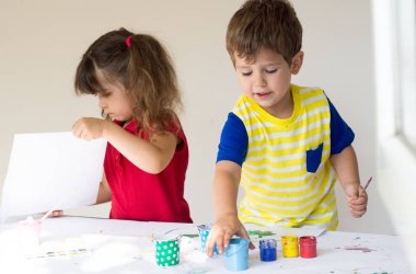 Sanat stüdyosu oynayan iki çocuklar. Dört yıl eski çocuk evde boyuyor. Boya fırçası ve suluboya ile güzel bir çocuk.