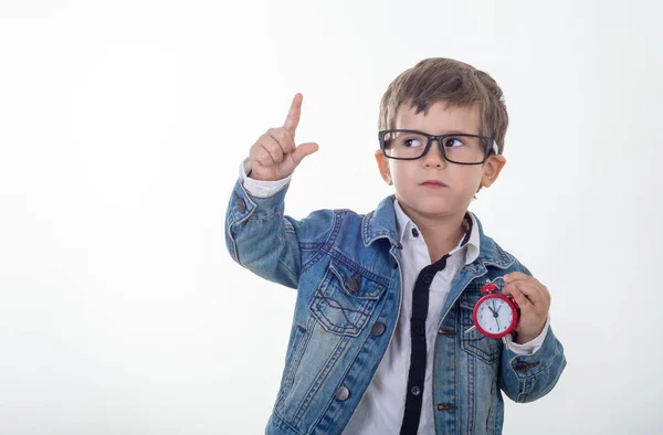 シャツとジーンズで幸せな若い男の子はジャケットと白い背景の上指を指している赤い時計を見上げると思考 子供の目覚まし時計 — ストック写真