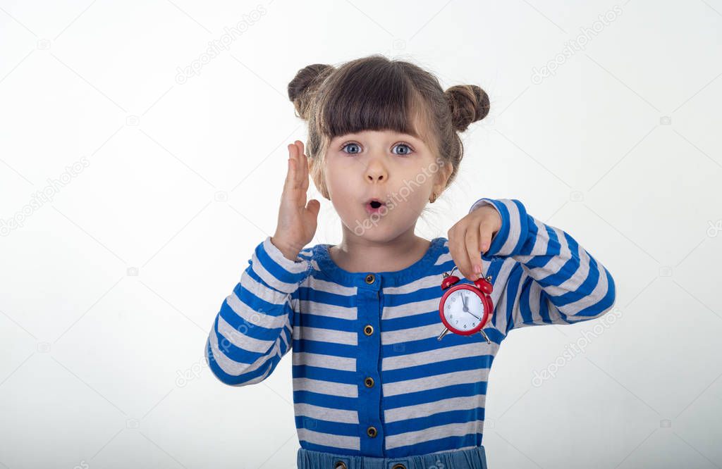 Surprised girl in dress with red clock on white background. Shocked kid holding alarm clock. Deadline or time-limit concept.