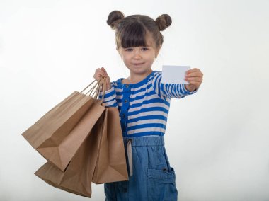 Mutlu çocuk beyaz indirim kartı ve alışveriş torbaları onun elinde tutan. Kredi kartı ile evlat. Boş boş kağıt Not kopya alanı gösterilen küçük kız. Beyaz arka plan.