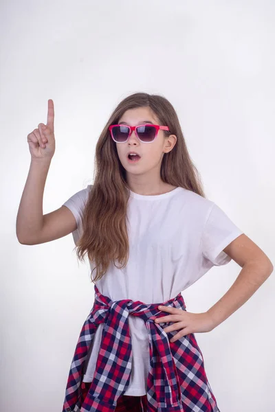 快乐的年轻女孩的肖像与太阳镜摆姿势 并在自由空间广告指指点点 白色背景 — 图库照片