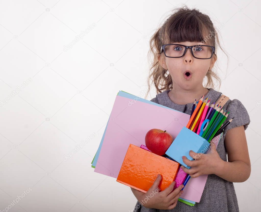 Shocked clever child in eyeglasses holding school supplies. Back to school concept. Space for text, isolated on white. Office supply objects collection.