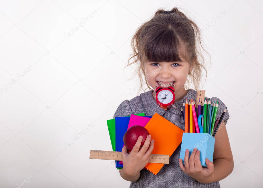 Kid ready for school. Cute clever child in eyeglasses holding school supplies: pens, notebooks, scissors, alarm clock and apple. Back to school concept. Space for text, isolated on white.