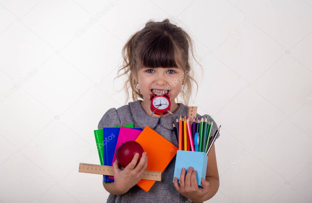 Kid ready for school. Cute clever child in eyeglasses holding school supplies: pens, notebooks, scissors, alarm clock and apple. Back to school concept. Space for text, isolated on white.