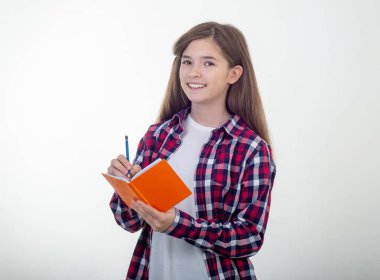 Genç kız kalem kullanarak ve gülümsüyor not defterinde yazılı. Öğrenci, üzerinde beyaz izole