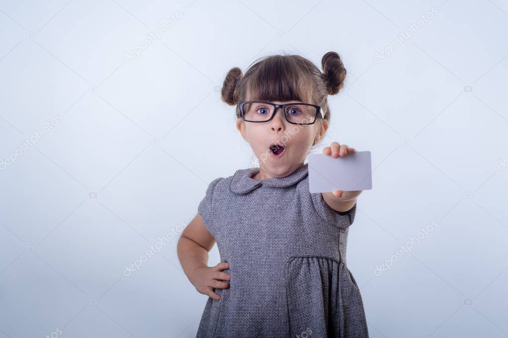 Cute smiling child with glasses showing bank card in her hands. Kid with credit card.  Isolated on blue background 