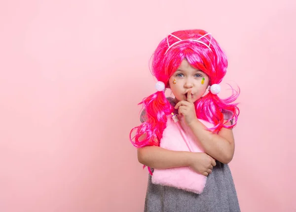 Keep silence gesture. Child with funny pink haircut put forefinger to lips as sign of silence, holding notepad. Pink background.