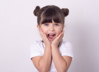 Headshot of impressed attractive little girl opening mouth from amazement and shock holding hands near face standing over white wall.  clipart