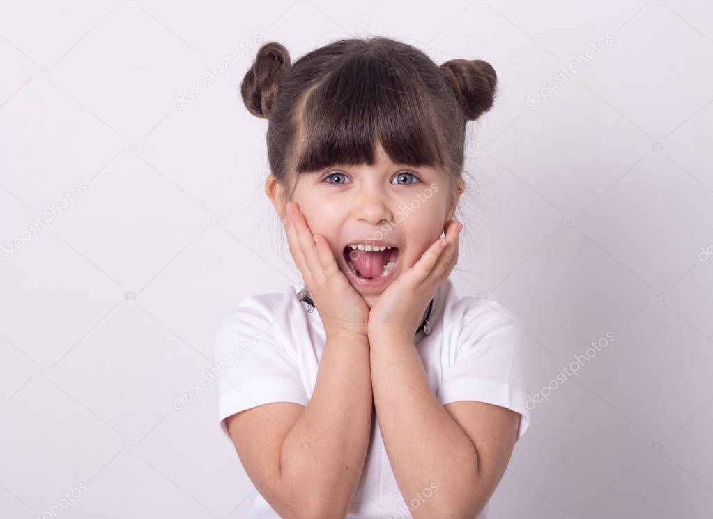 Headshot of impressed attractive little girl opening mouth from amazement and shock holding hands near face standing over white wall. 