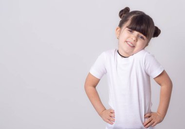 Güzel bir çocuk 5 yaşında omuzlarında shrugging ve kameraya bakarak beyaz t-shirt giyiyor. Beyaz arka plan üzerinde izole. 