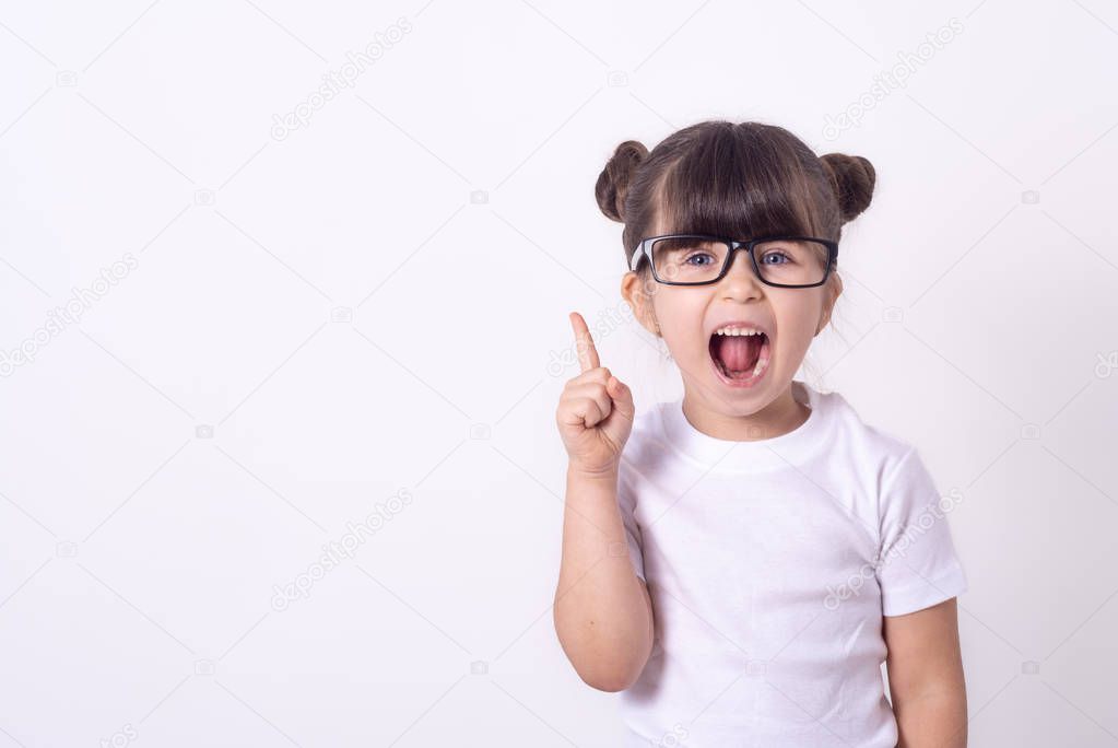 Indoor shot of friendly young girl laughing and smiling joyfully raising hands and pointing up showing copy space over grey background. Child  having an idea.
