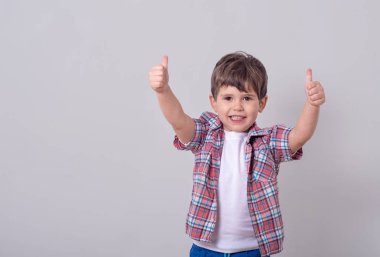 El ve göstermek thumbs up ile gri arka plan üzerinde izole ayakta sevimli çocuk çocuk resmi. Kamera bakıyor.