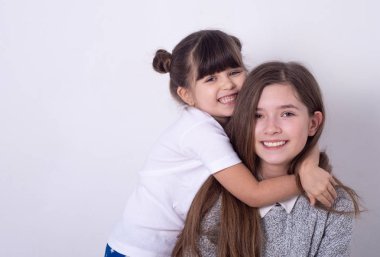 Genç kız kardeşler birbirlerine sarılıyorlar. İzole edilmiş, boş alan.