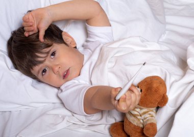 Yatakta ateşi ve hastalığı olan hasta çocuk termometre ile sıcaklığı kontrol ediyor. 