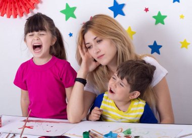 Tek anne gürültülü aktif yorgun baş ağrısı üzgün depresif hissediyor. Stresli ve yorgun anne. Ağlayan çocuklar ve genç anne.