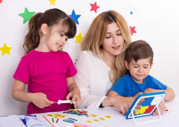Happy children learning to calculate with teacher at kindergarten, young woman and kids. 3 years old boy and 5 years girl learning numbers, mental arithmetic, abacus calculation. Back to school