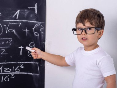 Okula geri dön. Gözlüklü komik küçük çocuk tahtayı işaret ediyor. Eğitim kavramı. Tebeşirli çocuk