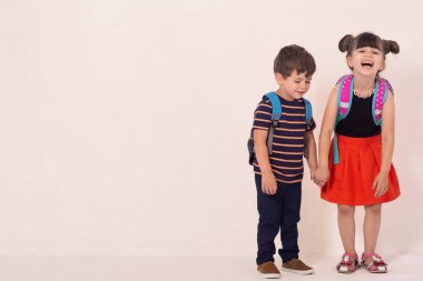 Sırt çantaları beyaz boş veya beyaz kart tutan Okul Çocukları. Mutlu çocuklar turuncu arka plan üzerinde izole okul için hazır. 