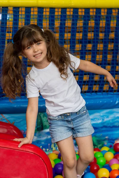 Playground with ball pit indoor. Joyful kid having fun at indoor play center. Child playing with colorful balls in playground ball pool. Holiday or birthday.