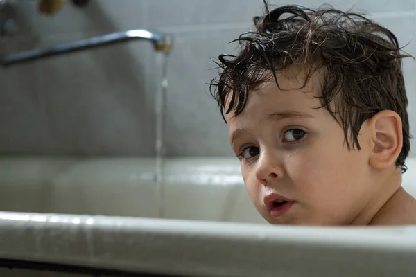 Happy funny kid laughing and bathed in the bath. Child washing in a bathroom indoors at home.