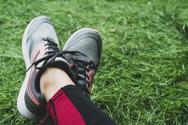 Fitness sport woman in fashion sportswear over green lawn background. Outdoor sports clothing and shoes, urban style. Sneakers closeup. Toned photo.