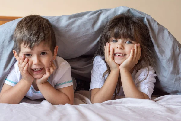 两个快乐的孩子睡觉前在床上玩得很开心 孩子们躺在毯子下躺在床上 面带微笑 — 图库照片