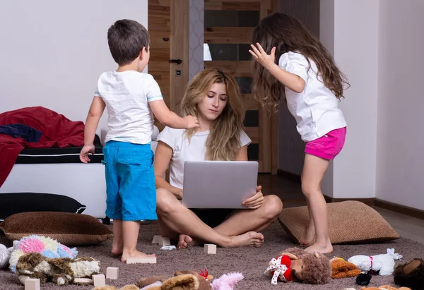 Şokta olan genç bir anne mutsuz çocuklarla bilgisayar üzerinde çalışıyor. Yorgun anne.