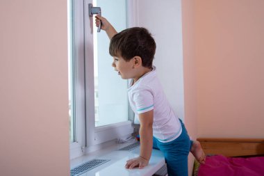 Pencereyi açmaya çalışan bir çocuk kolunu çekiyor. Çocuk Güvenliği. Ana Sayfadaki Pencere Kısıtlayıcıları.  