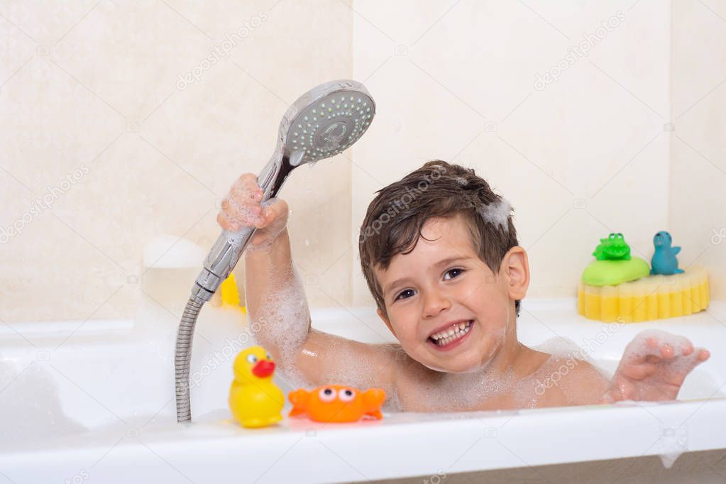 Hygiene for infant and baby. Child playing with soap foam in home bathroom. Rubber duck in foam bath. 