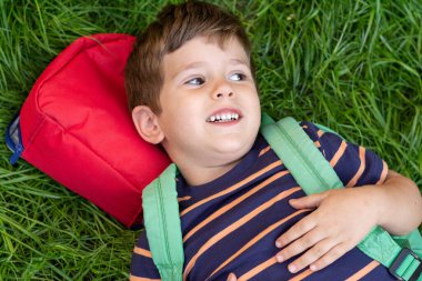 Gülümseyen beyaz, zeki, sarışın, küçük, çocuk yaşta, ilkokul öğrencisi, sırt çantalı, küçük bir çocuk. 