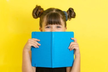 Şok olmuş çocuk yüzünü kitapla örterek, gözleri açık arkasına saklanıyor. İlkokulda, kitap okurken.