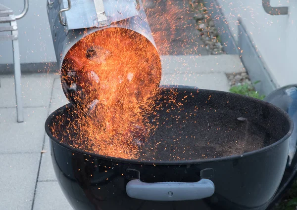 Pouring coal into a barbecue from a can, with lots of fire and red sparks.