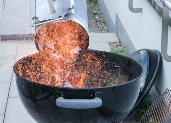 Putting coal into a barbecue, with lots of fire and sparks everywhere.