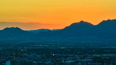 Las Vegas Nevada 'nın hava manzarası şehir merkezindeki canlı bir şeridi ve altın saatle çevreleyen dağları sergiliyor. Sıcak günbatımı tonlarıyla ve enerjik şehir atmosferiyle..